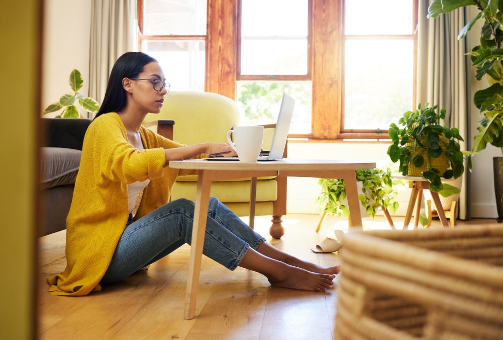 Focused woman working remotely sitting on the floor at a coffee table in a living room. A serious y